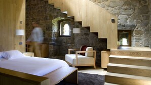 A bedroom with a wooden bed, a chair, and a staircase against a stone wall. - Rusticae Hotel Torre de Villademoros (Valdes)
