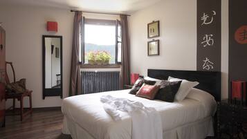 A neatly made bed with white linens, a window with a view of mountains, and a red chair.