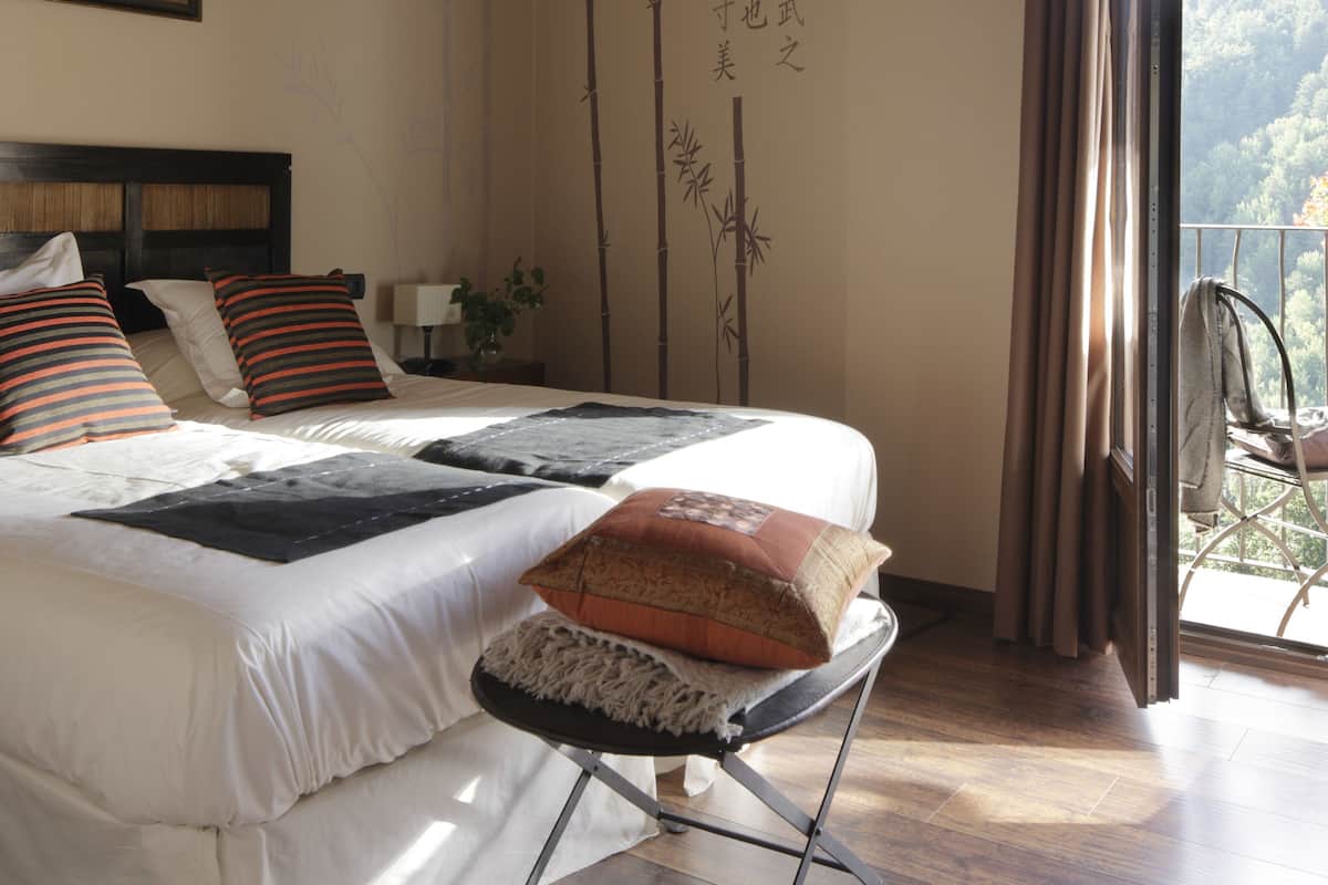 Une chambre avec un plafond en bois, un lit avec des coussins à rayures, une table de chevet avec une lampe, et une vue sur un balcon avec une chaise.