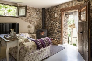 Una habitación acogedora con pared de piedra, chimenea, cama con ropa de cama floral y puerta de madera.