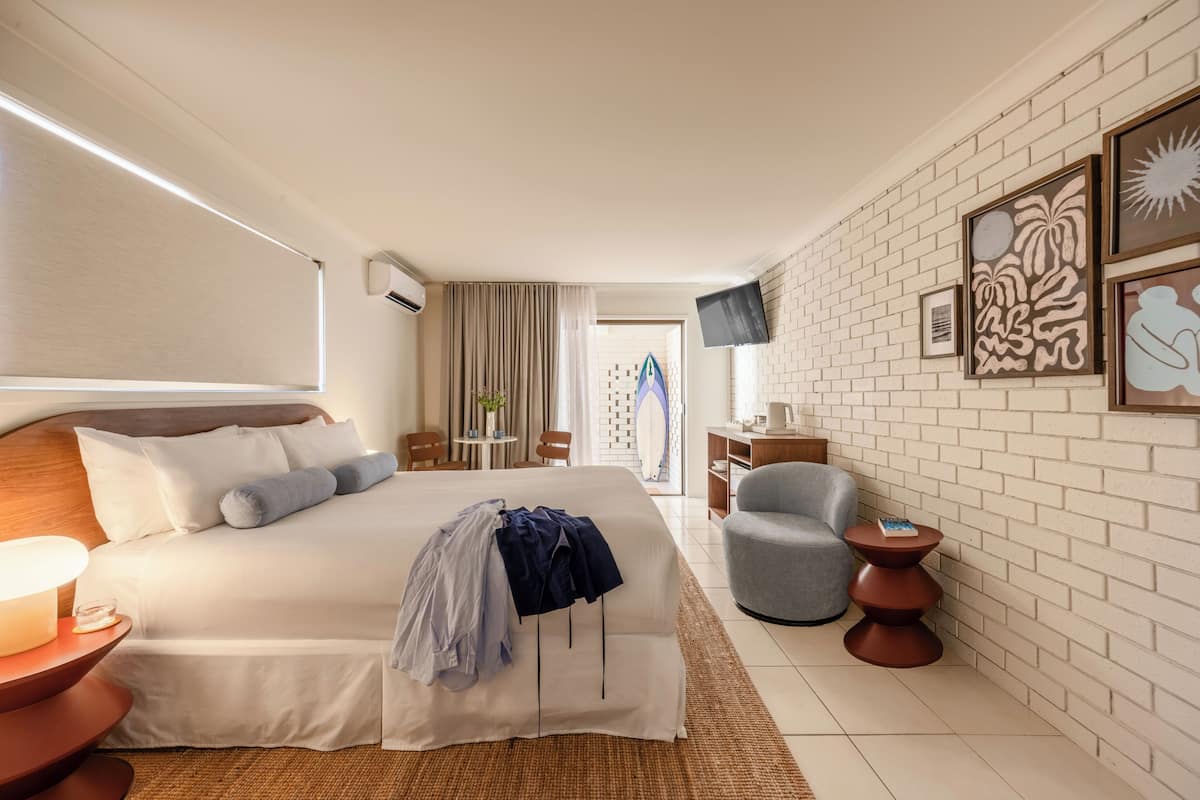 Une chambre d’hôtel avec un lit, une télévision, une chaise, une petite table et des œuvres d’art accrochées au mur.