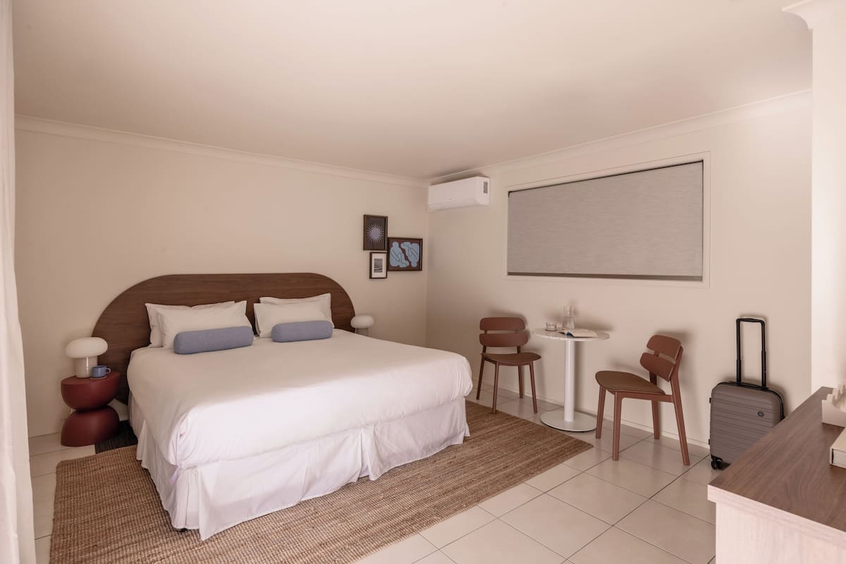 Une chambre d’hôtel avec un grand lit, une petite table, deux chaises, un bureau et une valise.