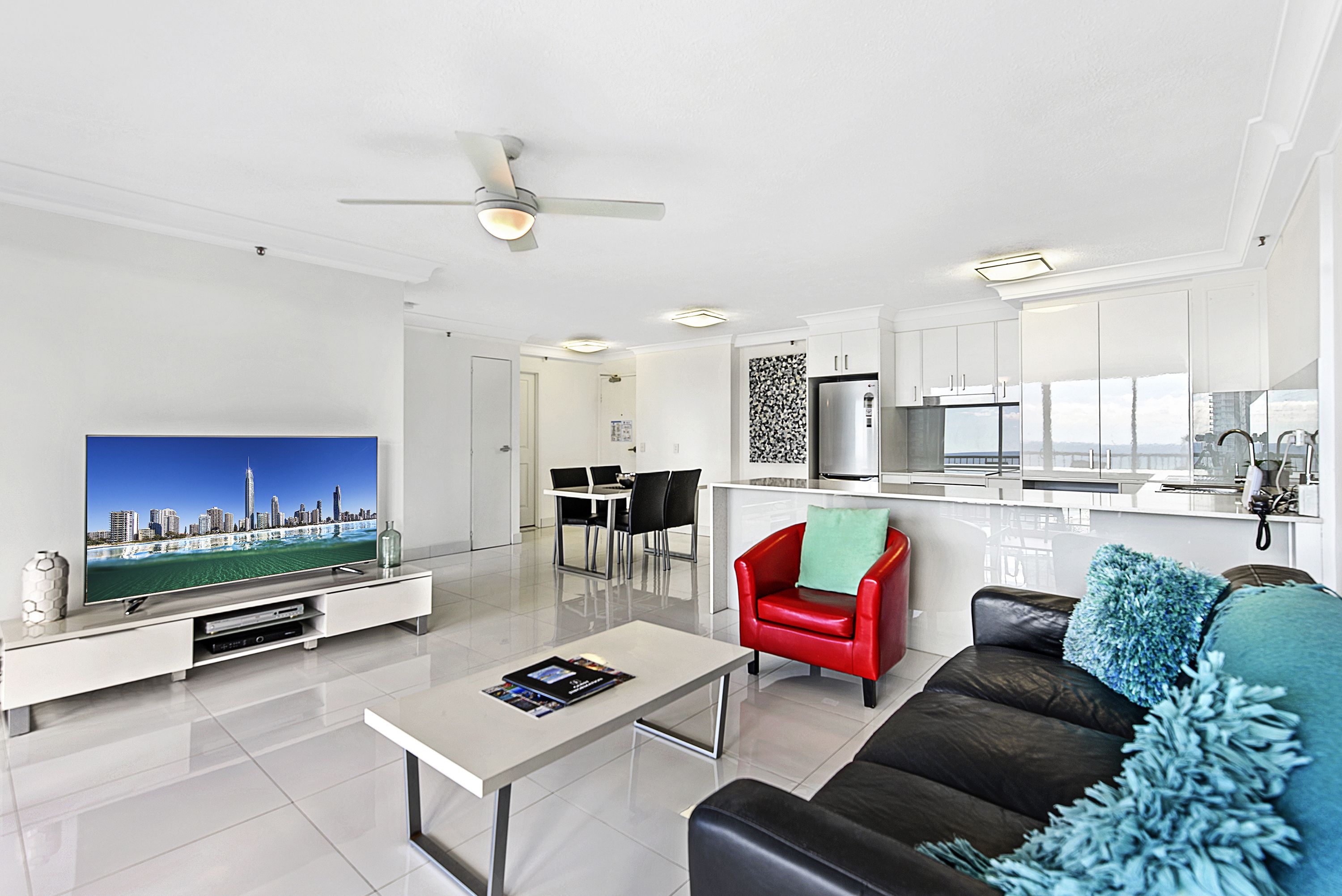 A modern living room with a flat-screen TV, a coffee table, a red chair, and a black sofa.