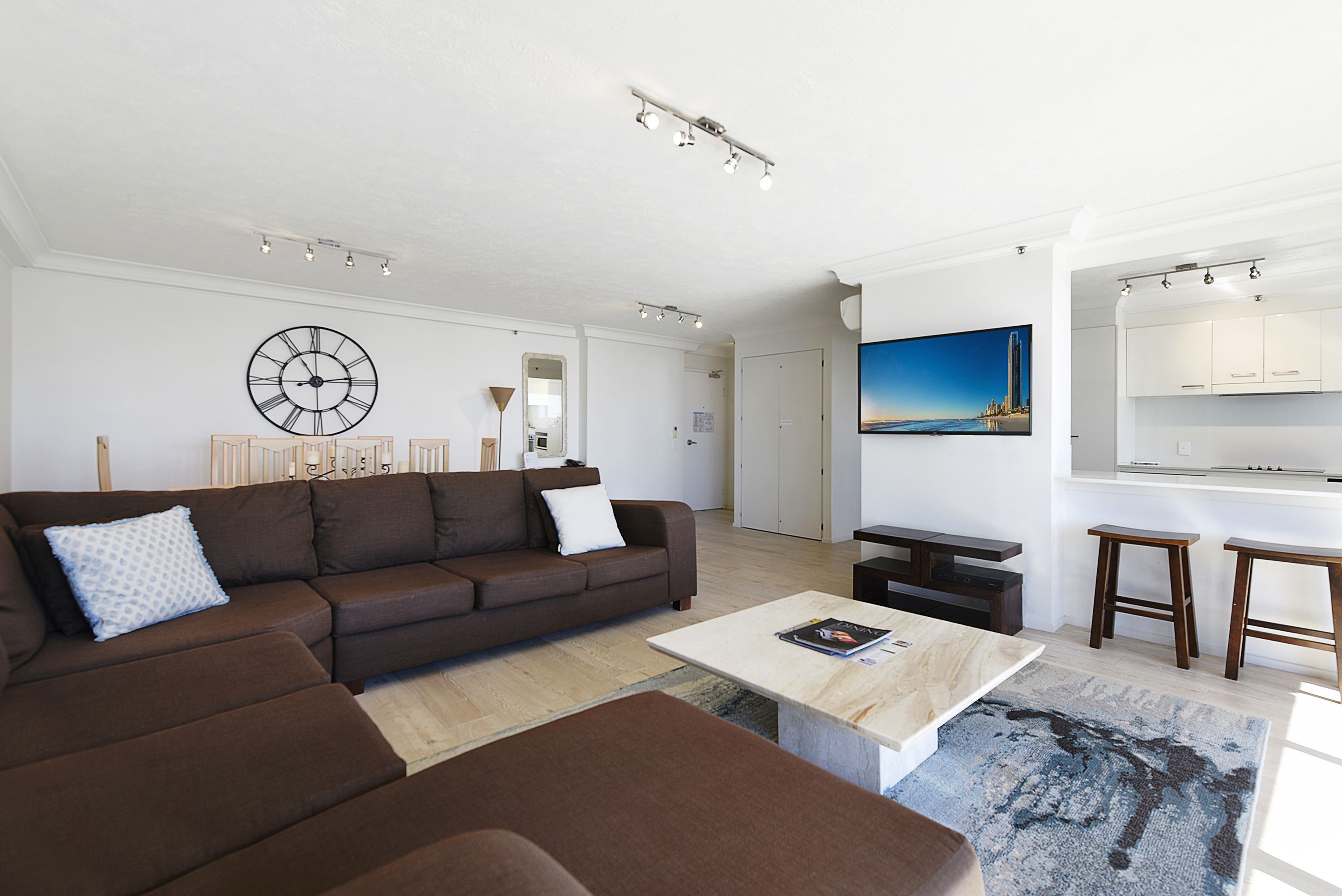 En moderne stue med en brun sofa, et sofabord og et fjernsyn ophængt på væggen.