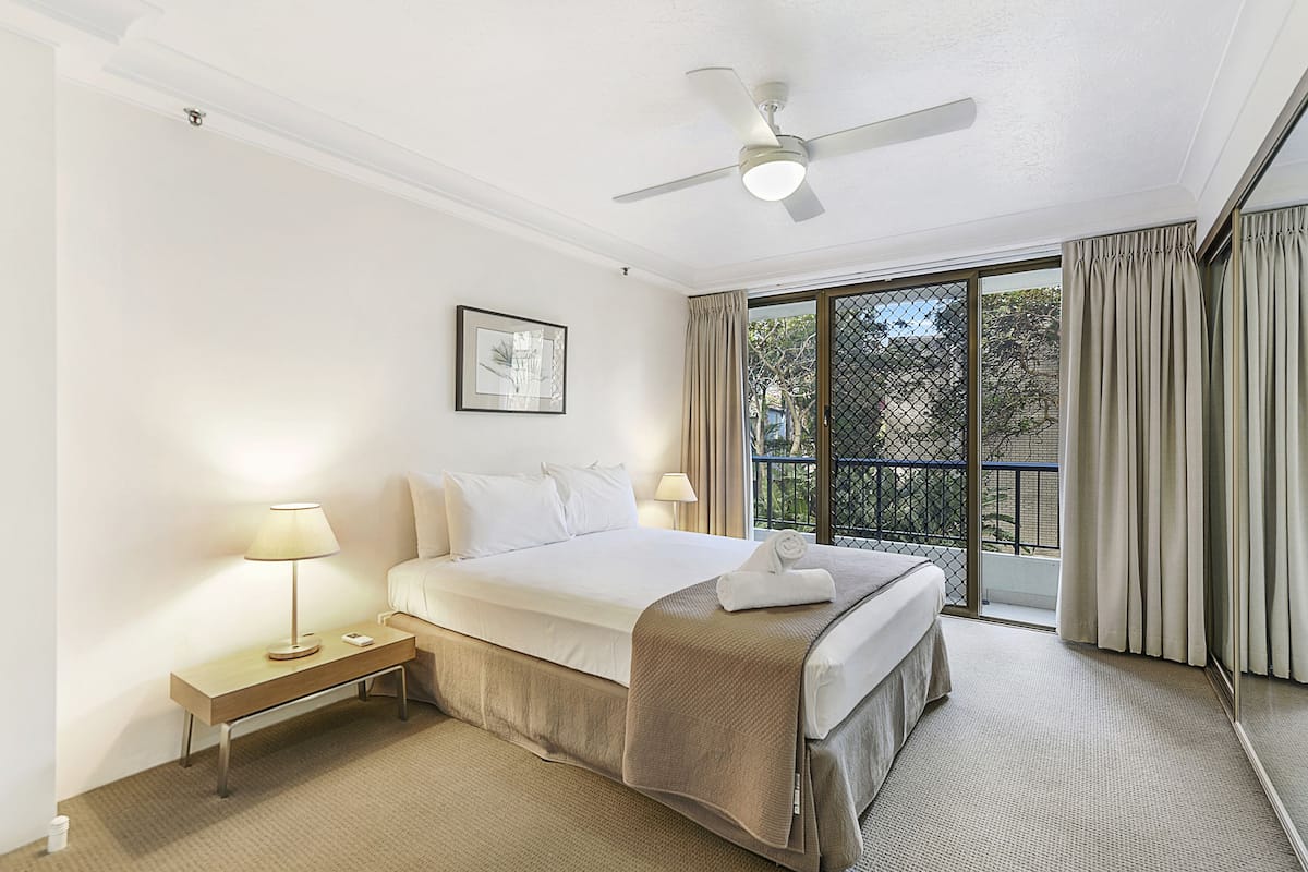 Una habitación de hotel con cama, mesita de noche, lámpara y ventilador de techo.