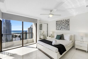 Een moderne hotelkamer met een groot bed, een plafondventilator, uitzicht op de oceaan en een stadsgezicht.