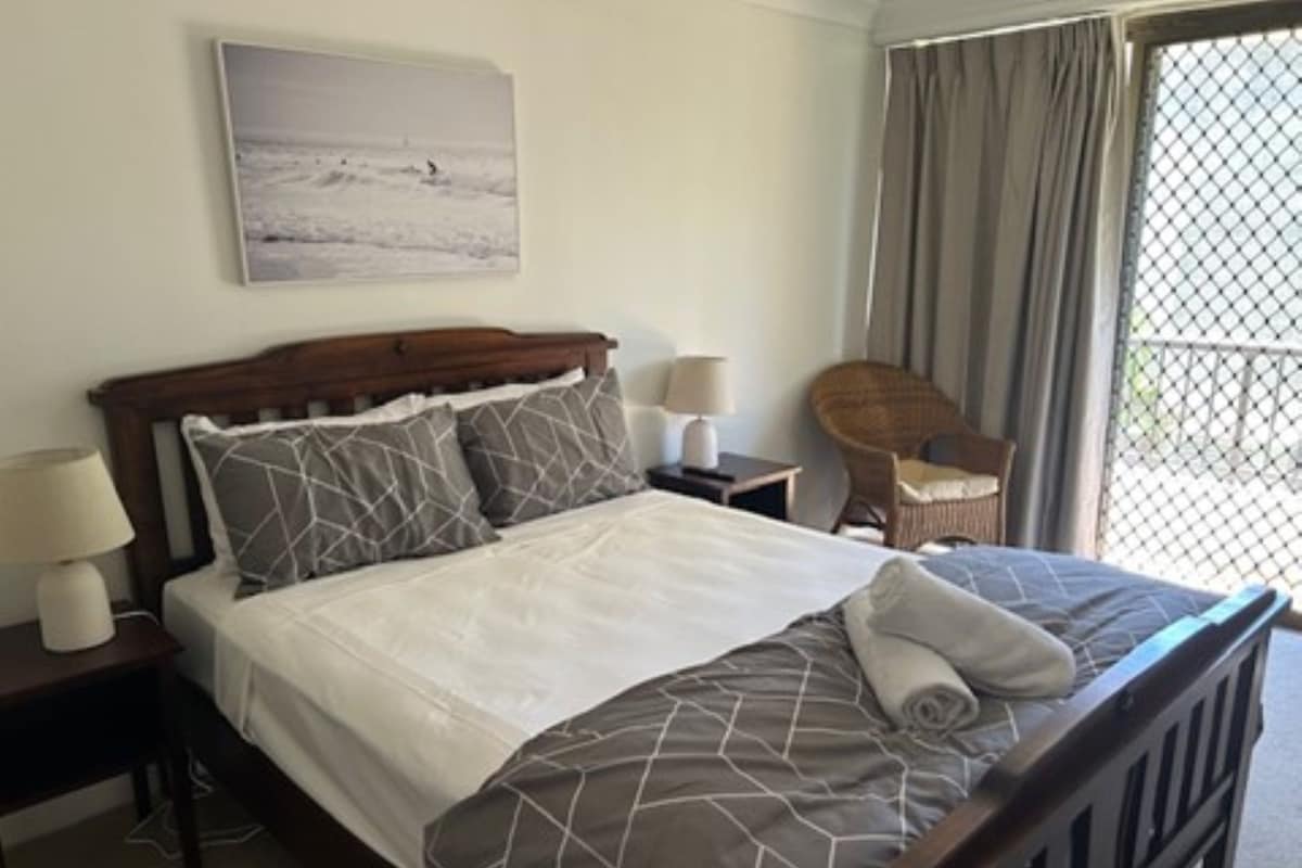 Une chambre d’hôtel avec un lit, une chaise, une table de chevet et une fenêtre avec des rideaux.