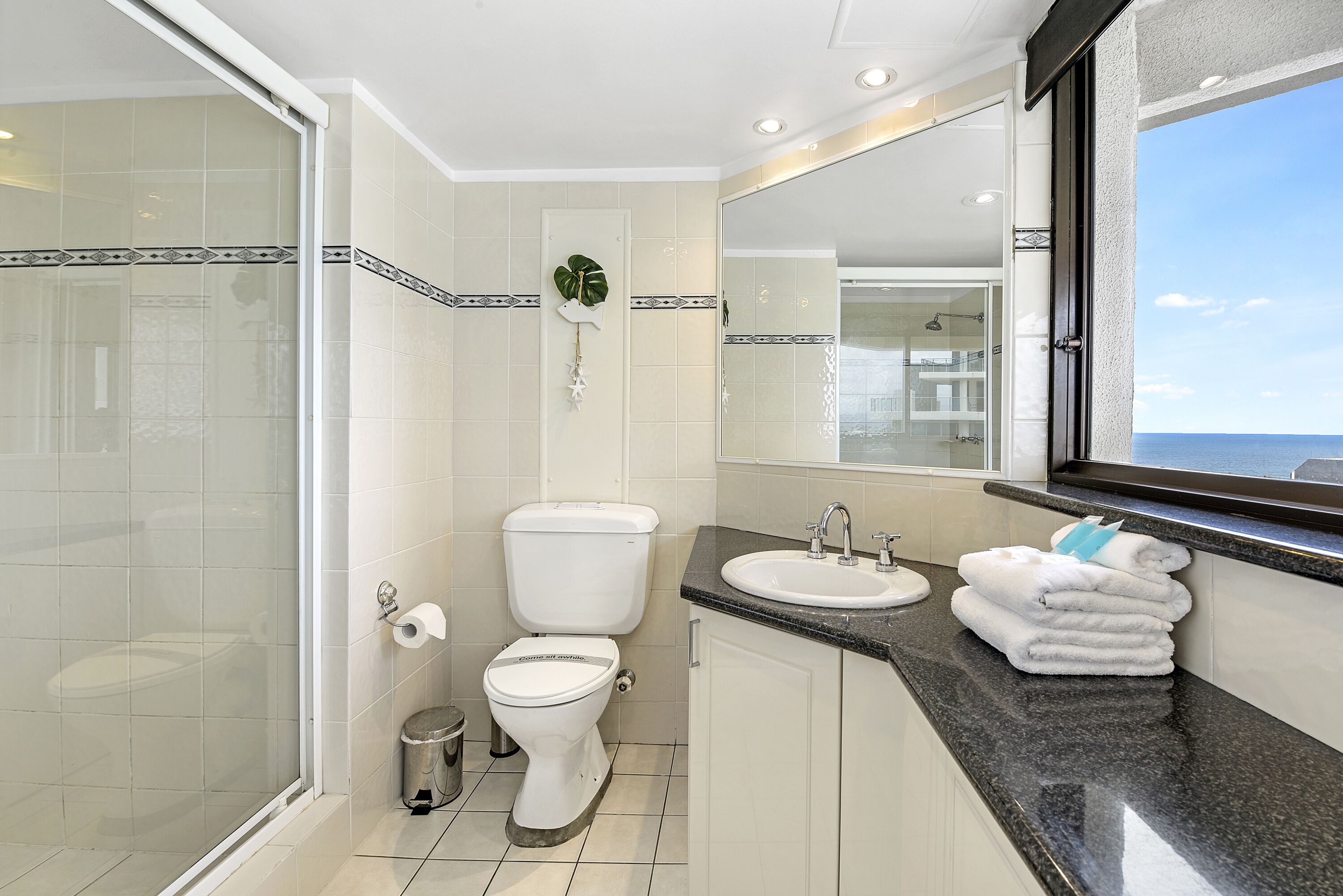 Un baño moderno con cabina de ducha de vidrio, inodoro, lavabo y un espejo grande.