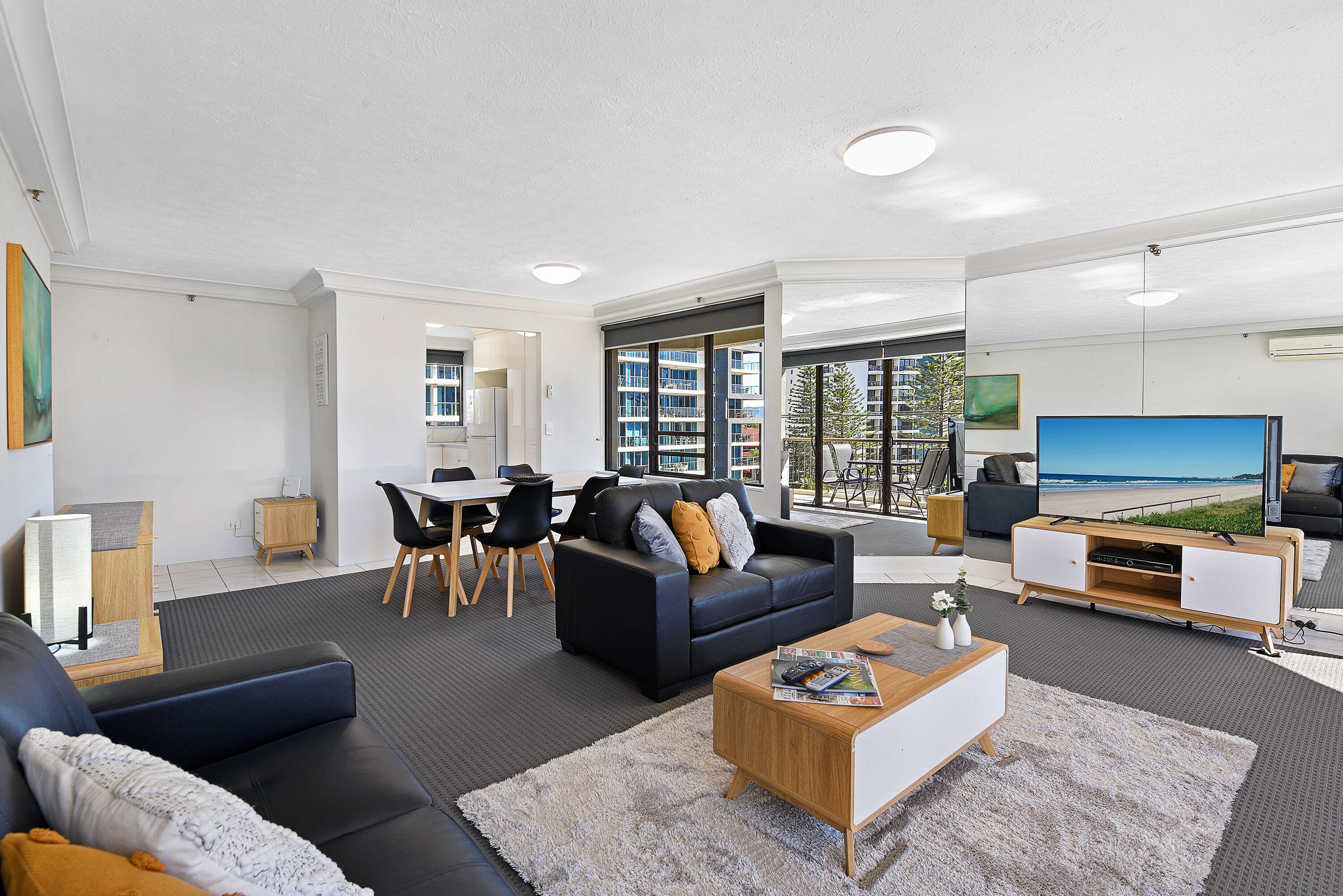 A modern living room with a black leather sofa, a wooden coffee table, and a large flat-screen TV.
