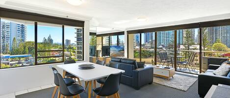A modern living room with a dining area, large windows, and a view of the city.
