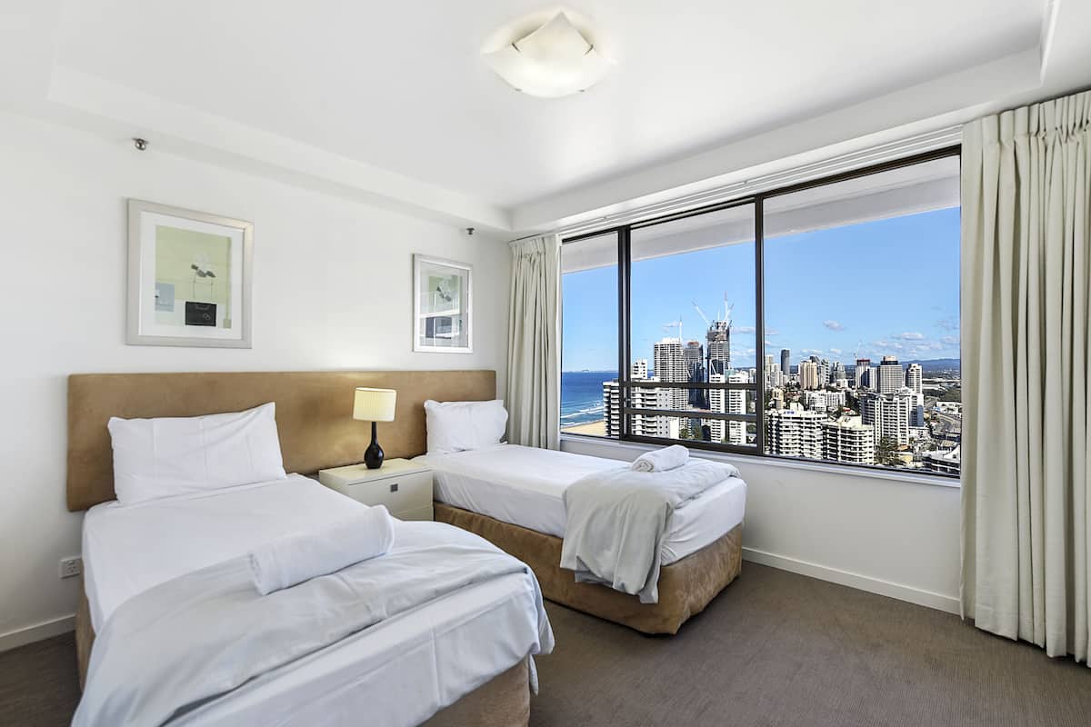 Habitación de hotel con dos camas, un ventanal grande con vistas a la ciudad y una lámpara en el techo.