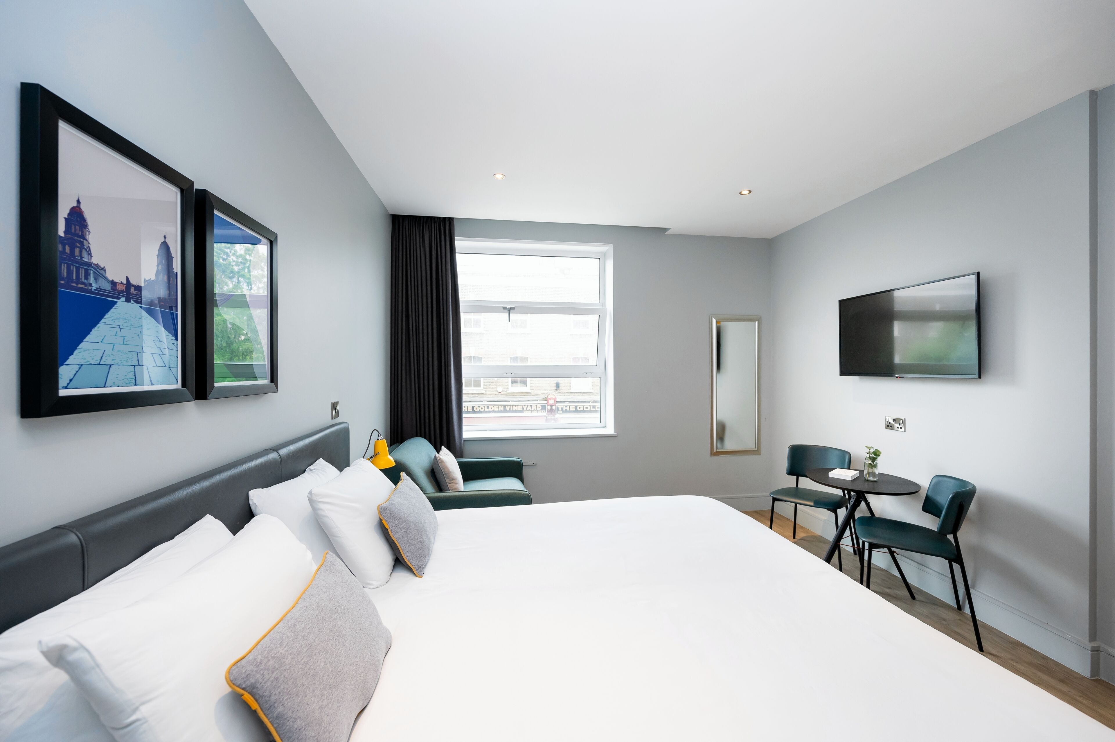 Una habitación de hotel moderna con una cama grande, un escritorio con dos sillas, una ventana con vistas y obras de arte en las paredes.