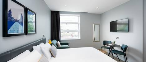 Una habitación de hotel moderna con una cama grande, un escritorio con dos sillas, una ventana con vistas y obras de arte en las paredes.