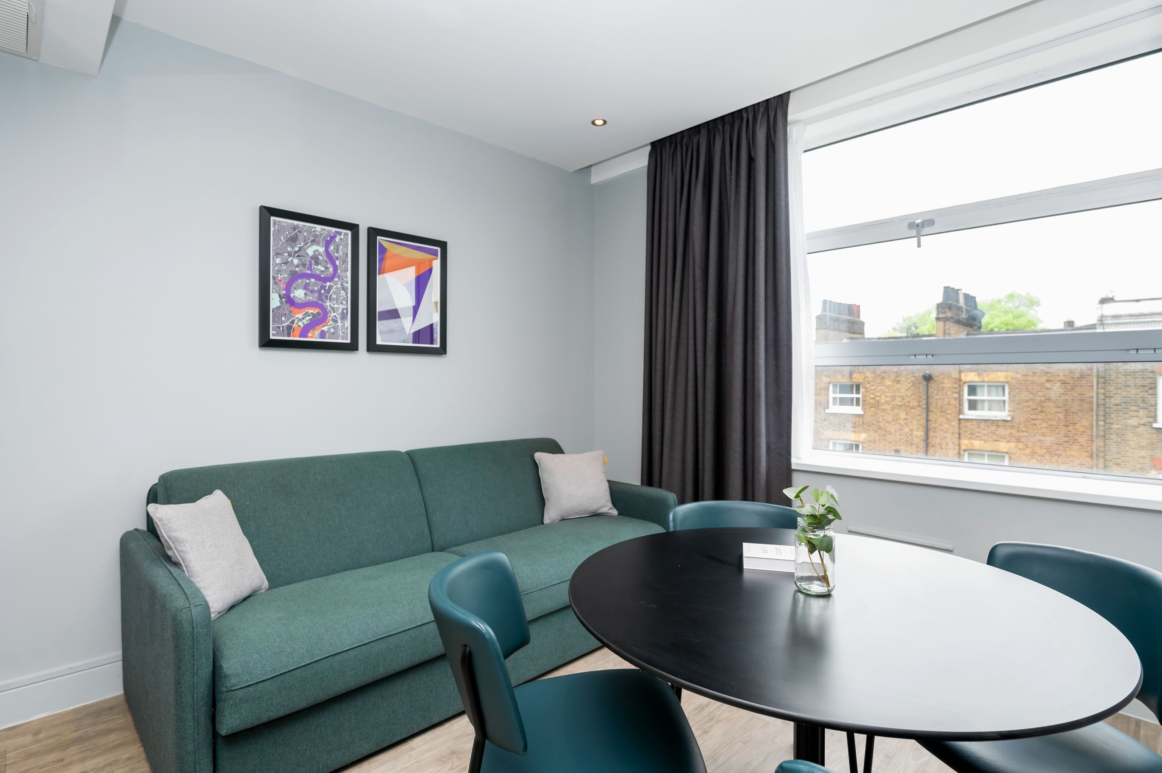 A modern room with a green sofa, two chairs, a round table, and two abstract paintings on the wall.