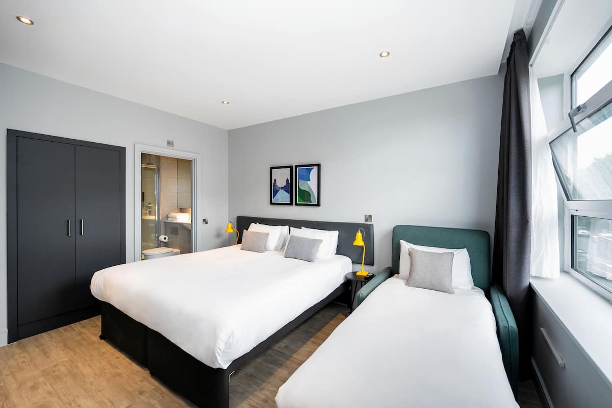 Une chambre d’hôtel avec deux lits, une armoire, un miroir, une table de chevet et une fenêtre avec des rideaux.