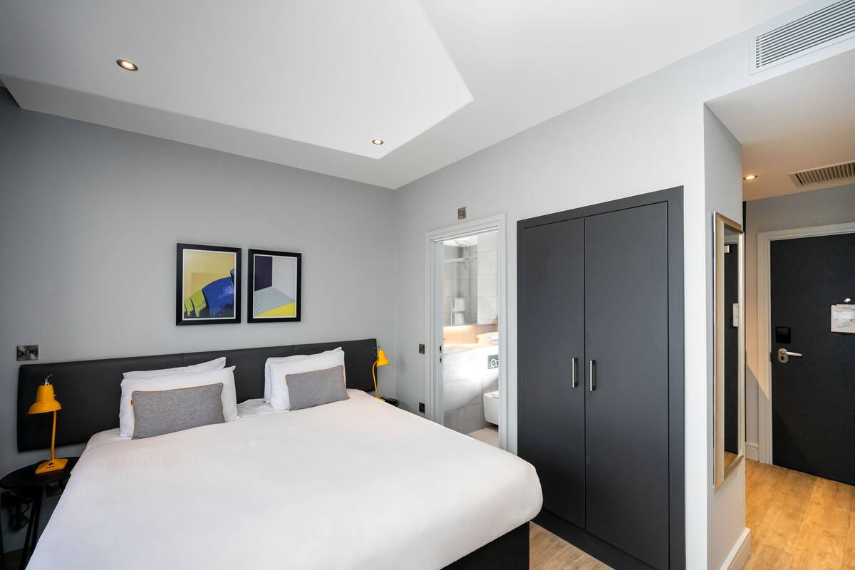 Une chambre d’hôtel moderne avec un grand lit, une armoire et une salle de bain visible à travers une porte ouverte.