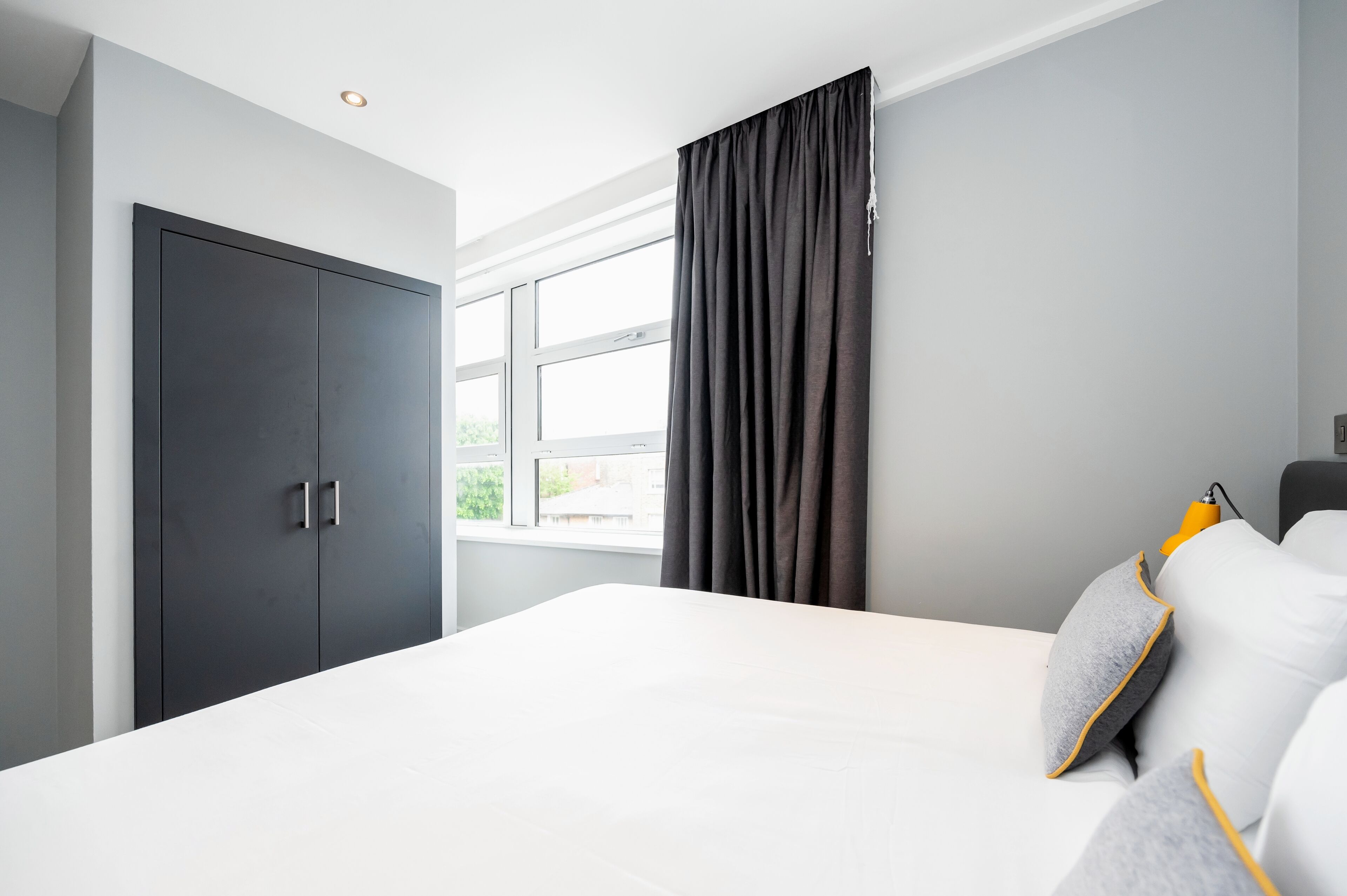 A modern bedroom with a large bed, a wardrobe, and a window with curtains.