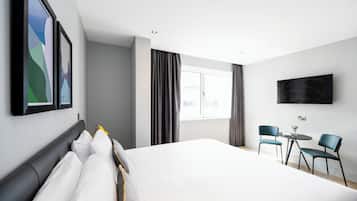 Habitació d'hotel moderna amb un llit gran, una televisió i una zona de seients amb dues cadires i una taula petita.