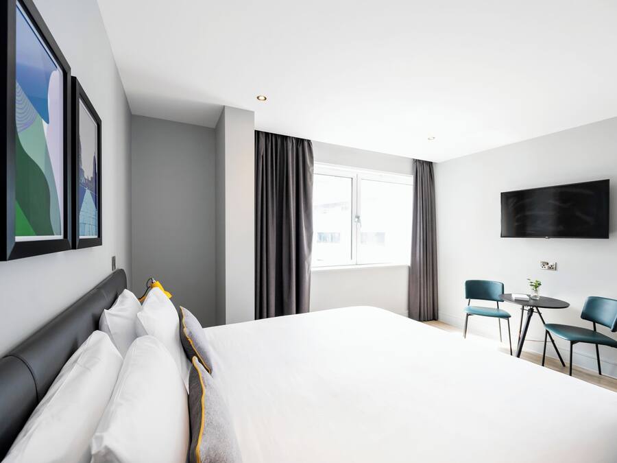 Habitació d'hotel moderna amb un llit gran, una televisió i una zona de seients amb dues cadires i una taula petita.