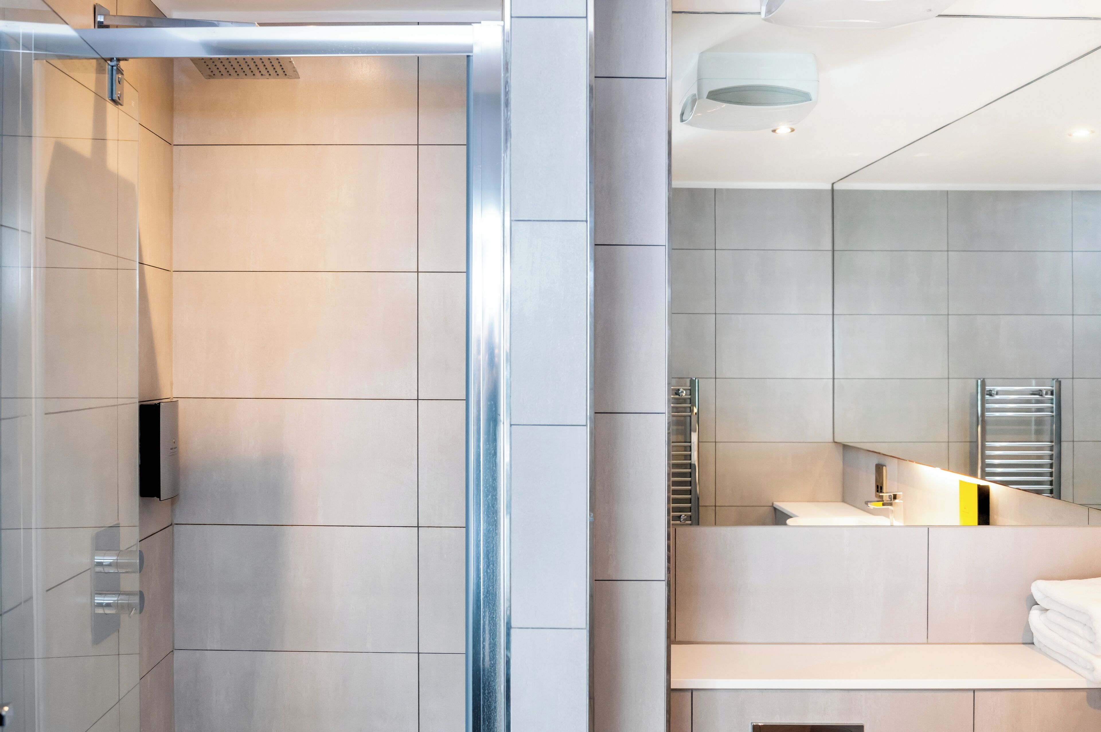 A modern bathroom with a glass shower enclosure, a large mirror, and a built-in towel rack.