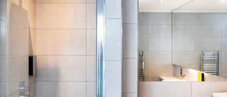 A modern bathroom with a glass shower enclosure, a large mirror, and a built-in towel rack.