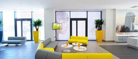 A modern lobby with yellow and gray seating, large windows, and a digital screen.