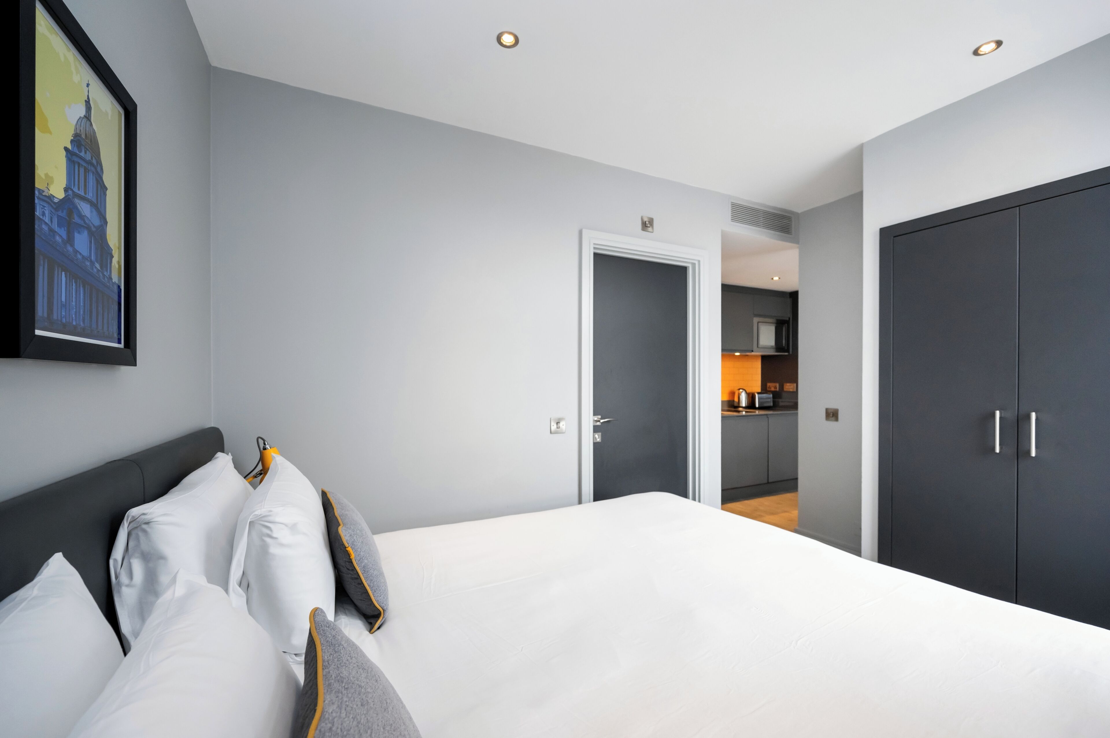 Een moderne hotelkamer met een groot bed, een donkere kast en een keukenruimte zichtbaar door een geopende deur.