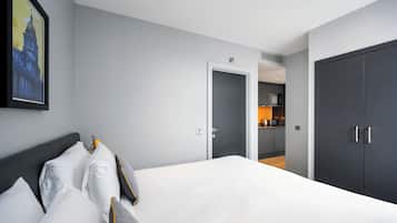 A modern hotel room with a large bed, a dark wardrobe, and a kitchen area visible through an open door.
