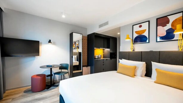 Una habitación de hotel con cama, escritorio, silla, una mesita y televisor.