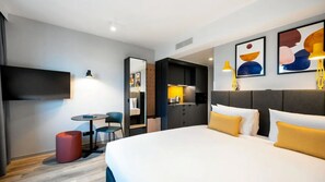 Habitació d'hotel amb un llit, una taula de nit, una cadira, una taula petita i una televisió.