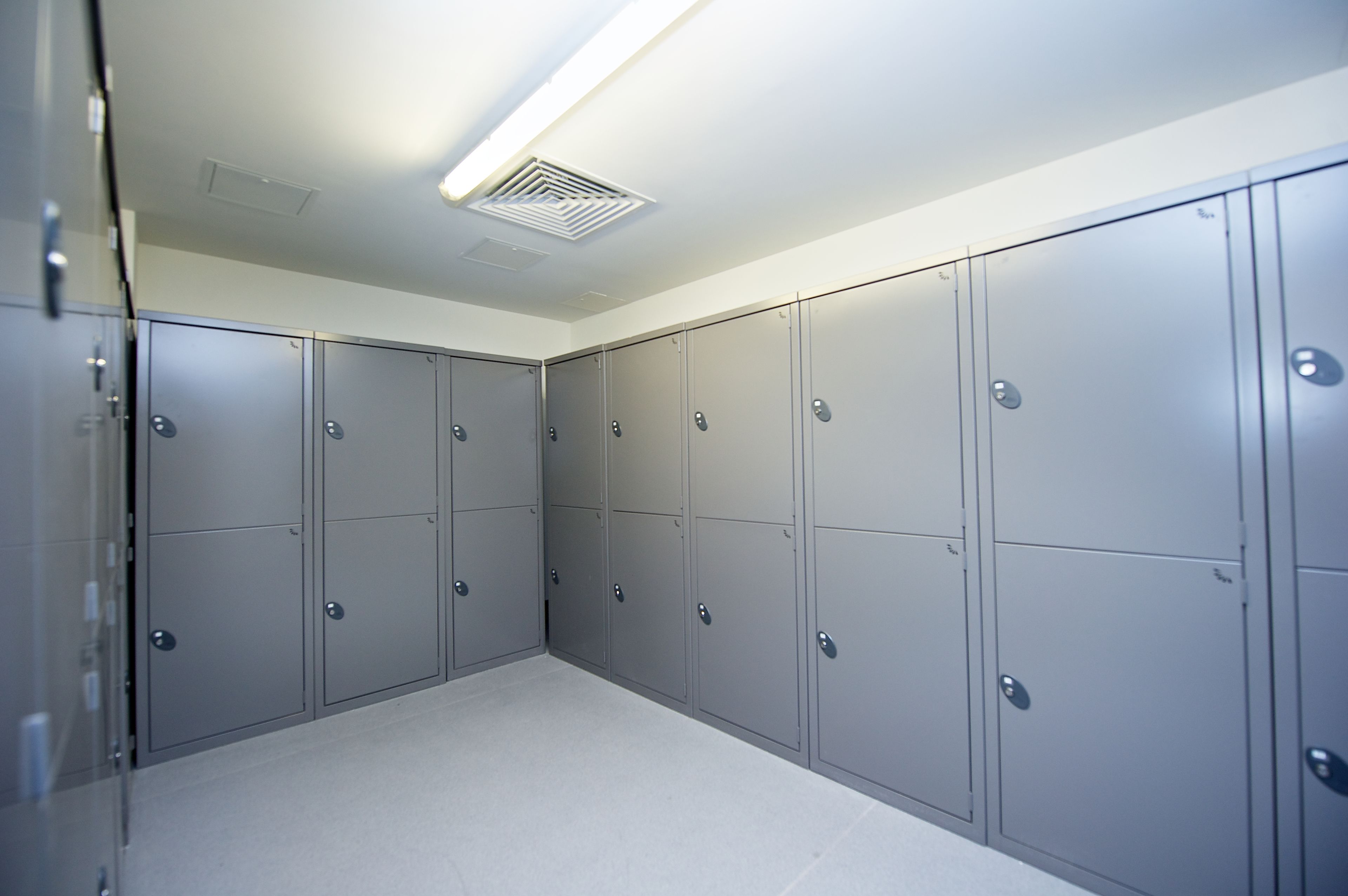 A clean, modern locker room with grey lockers and a bright ceiling light.