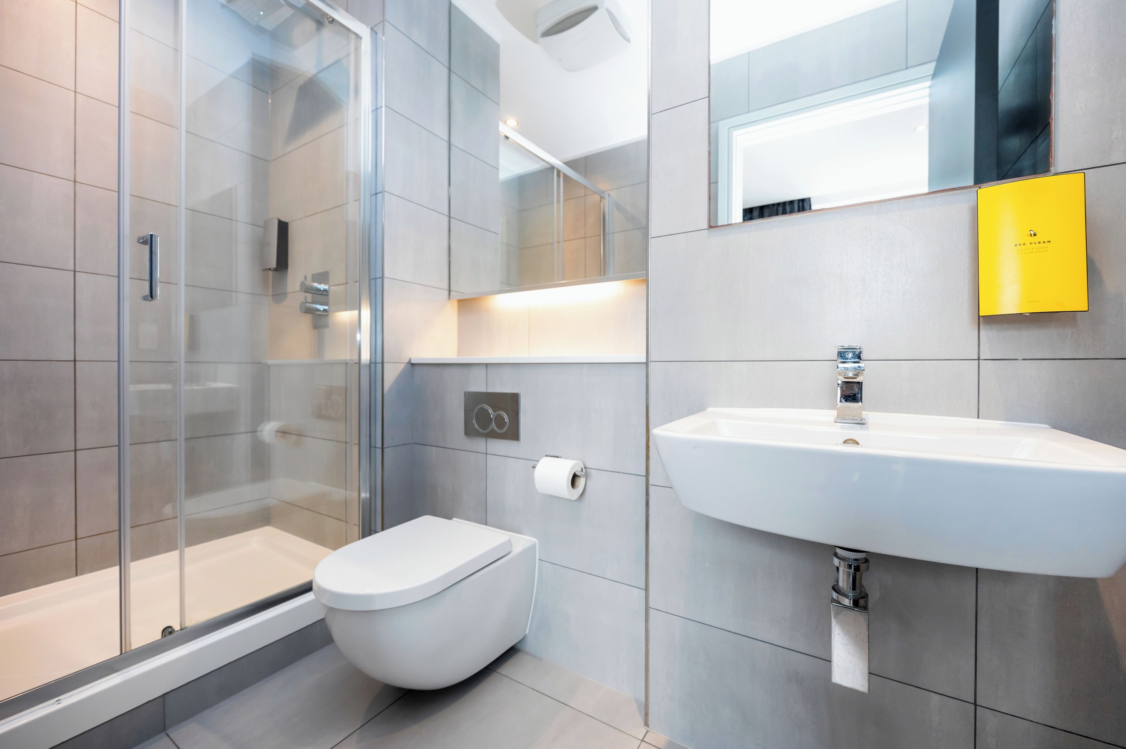 A modern bathroom with a glass-enclosed shower, a white toilet, and a sink with a mirror above it.