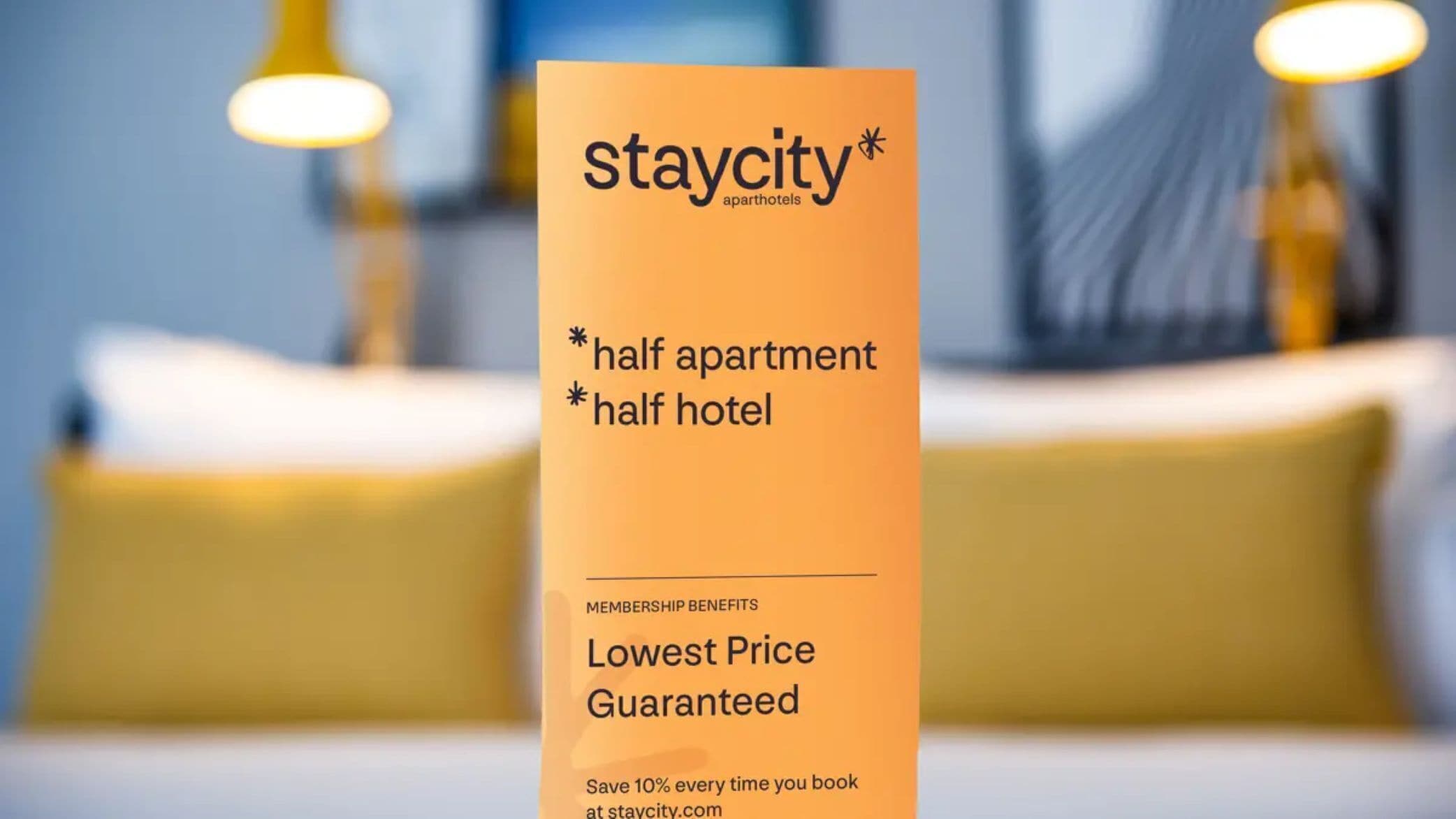 A staycity apartment/hotel sign with a blurred background of a bed and pillows.