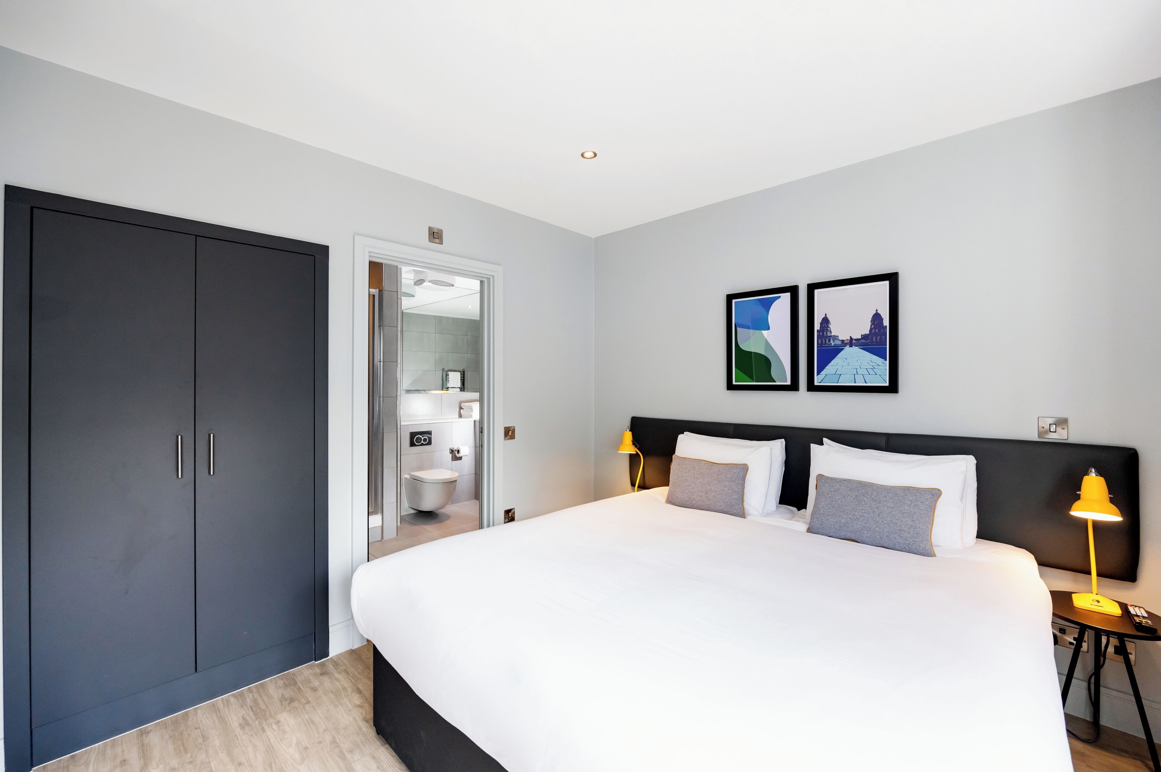 Una camera d'albergo moderna con un letto grande, un armadio, un bagno e due quadri appesi al muro.