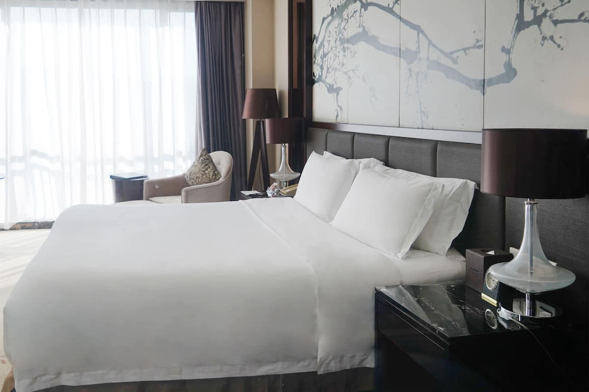 Une chambre d’hôtel avec un grand lit, une chaise, une table de chevet et une lampe.