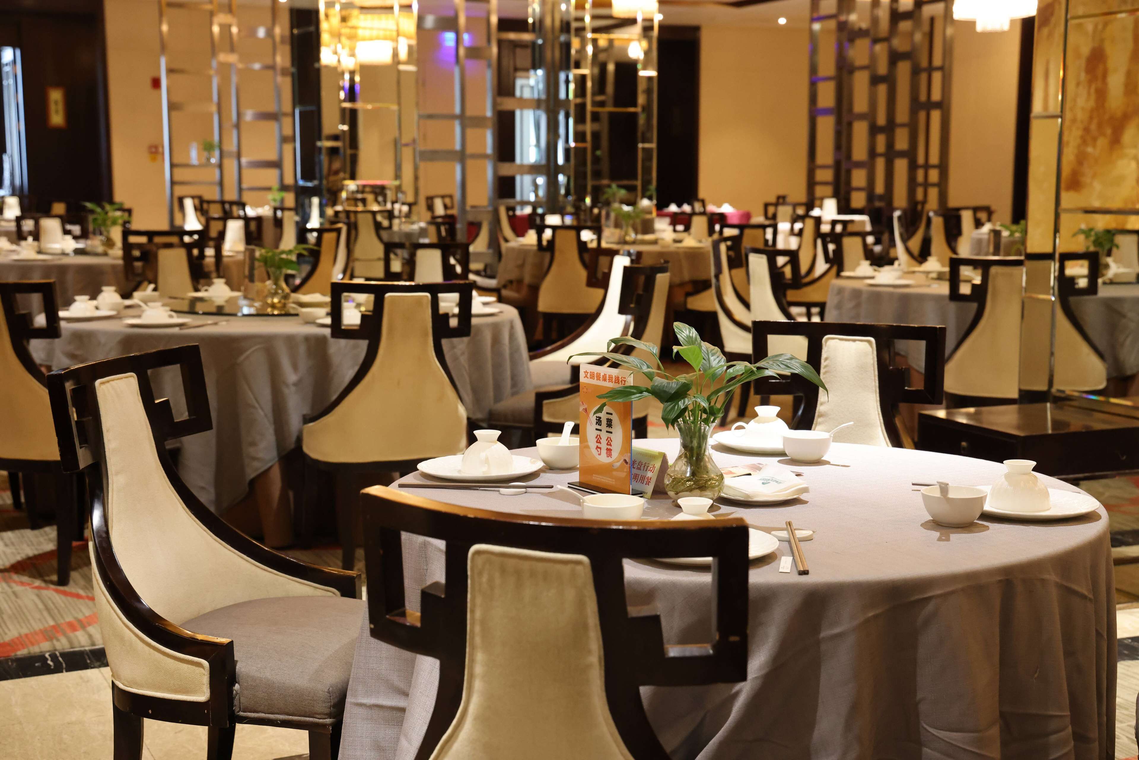 Une salle à manger bien éclairée, avec des tables rondes, des chaises et une variété d’articles de table, notamment des assiettes, des bols et des baguettes.