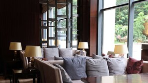 Une chambre d’hôtel moderne dotée d’une grande fenêtre, d’un ensemble de canapés et de deux tables d’appoint avec des lampes.