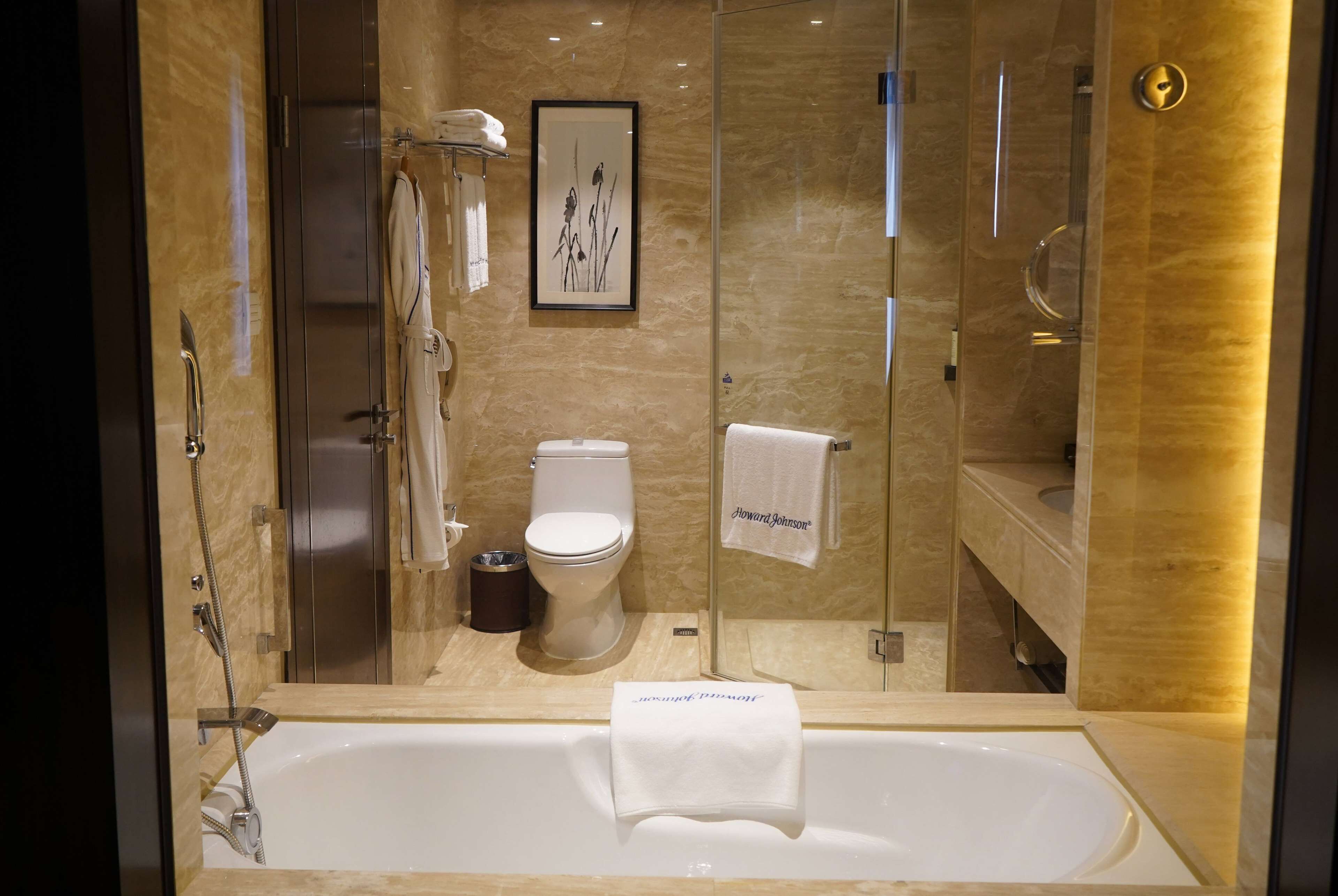 A modern bathroom with a glass-enclosed shower, a standalone toilet, and a bathtub with a towel hanging on the side.