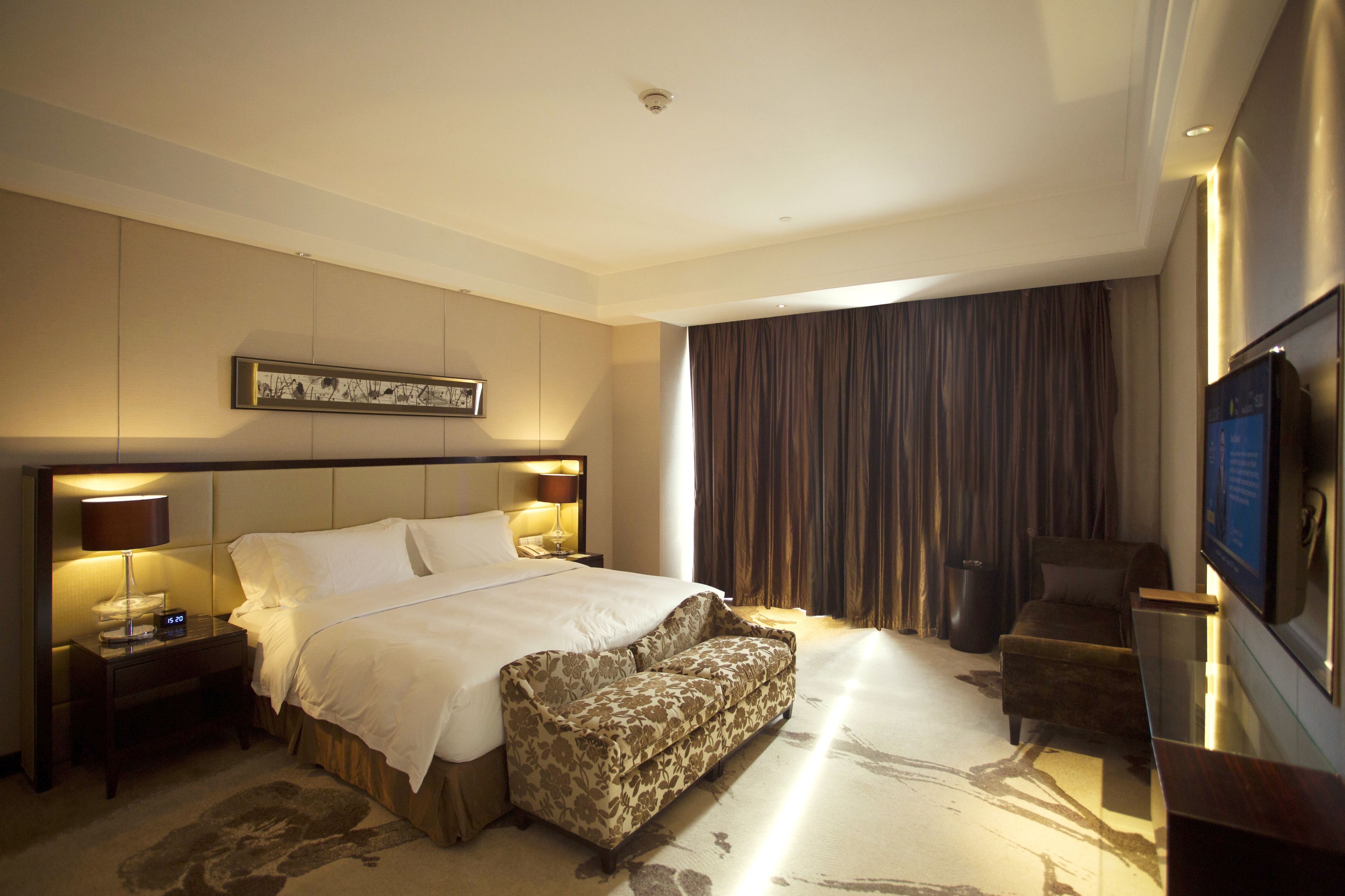 A hotel room with a large bed, a sofa, a TV, and a nightstand with a lamp.