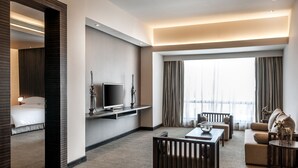 A modern hotel room with a bed, a TV, a sofa, a coffee table, and a large window with curtains. - Hyatt Raipur (Raipur)