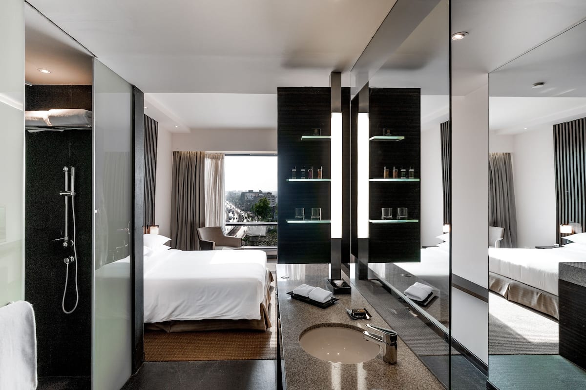 A modern hotel room with a large bed, a bathroom with a glass shower enclosure, and a view of the city through the window.