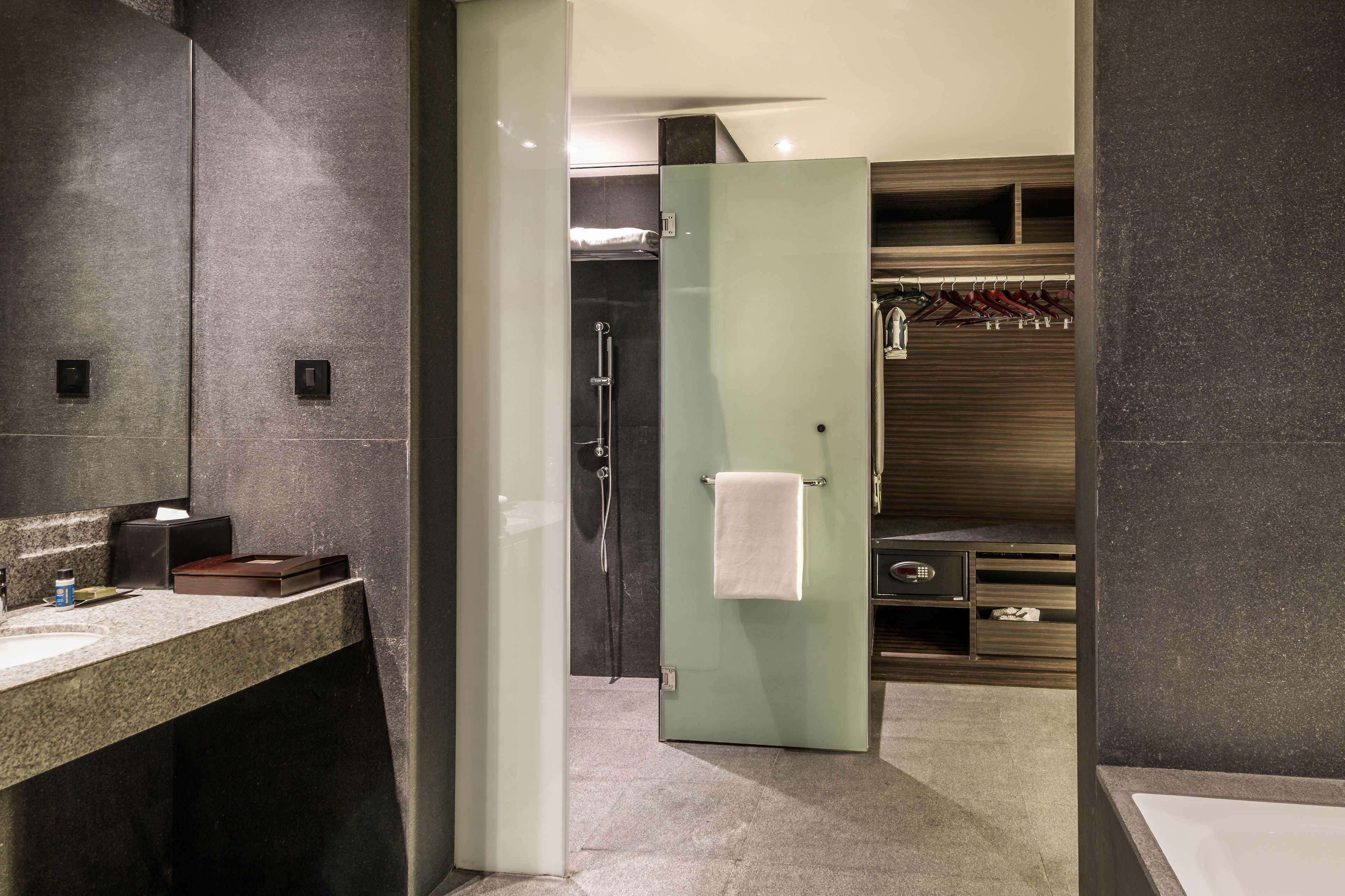 A modern bathroom with a granite countertop, a glass shower enclosure, and a walk-in closet with wooden shelves.