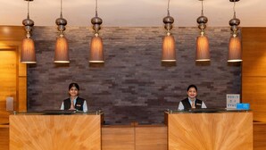 Una recepción con dos recepcionistas, una pared de madera con textura y lámparas colgantes.