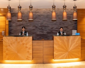 A reception desk with two attendants, a wooden wall with a textured pattern, and pendant lighting. - Hyatt Raipur (Raipur)