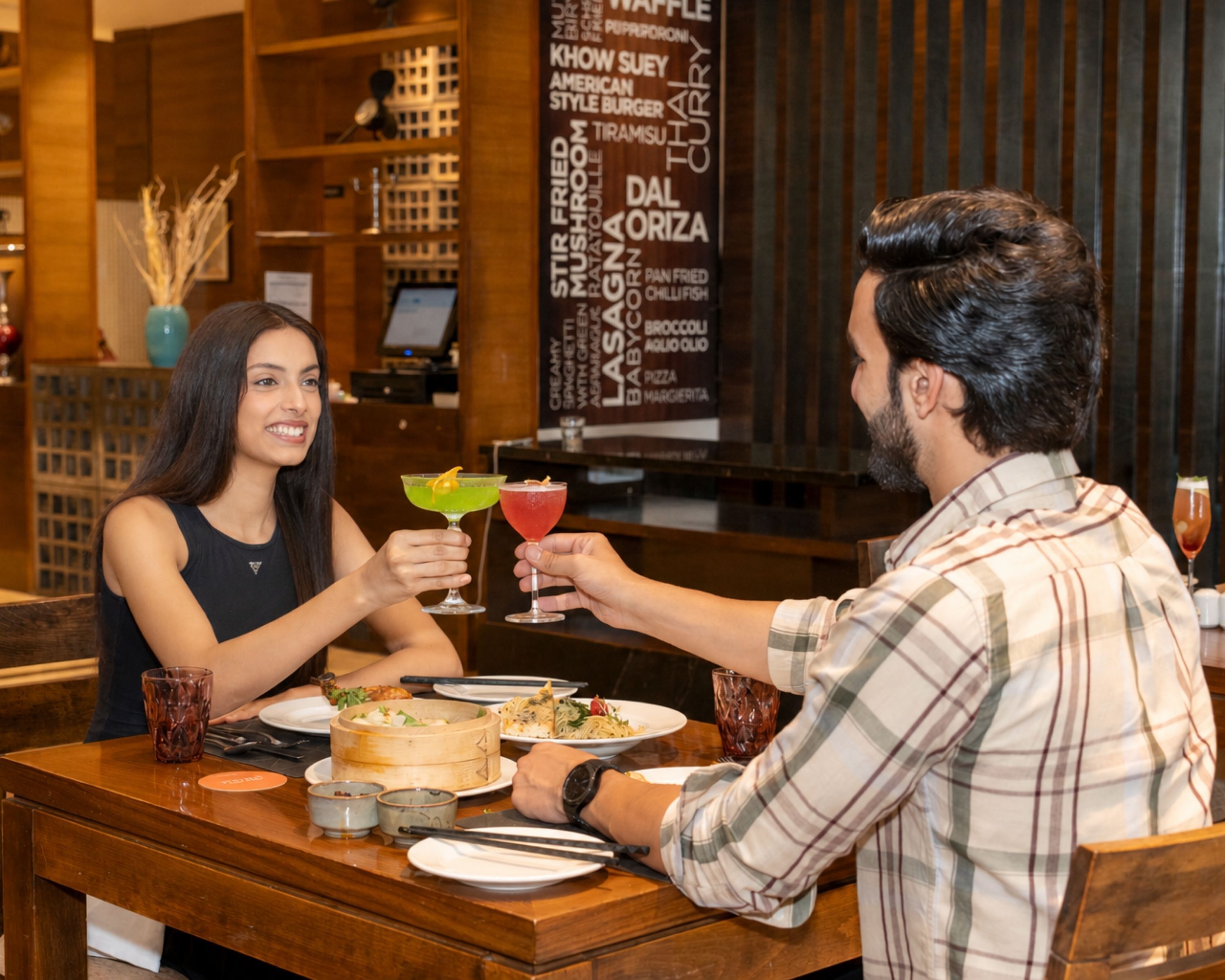 A restaurant interior with a menu board, wooden furniture, and a dining table with food and drinks.