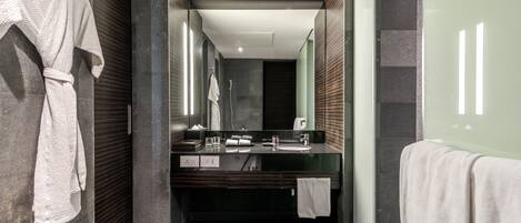 A modern bathroom with a large mirror, dark tiles, a bathtub, and a vanity with a sink and towel rack.