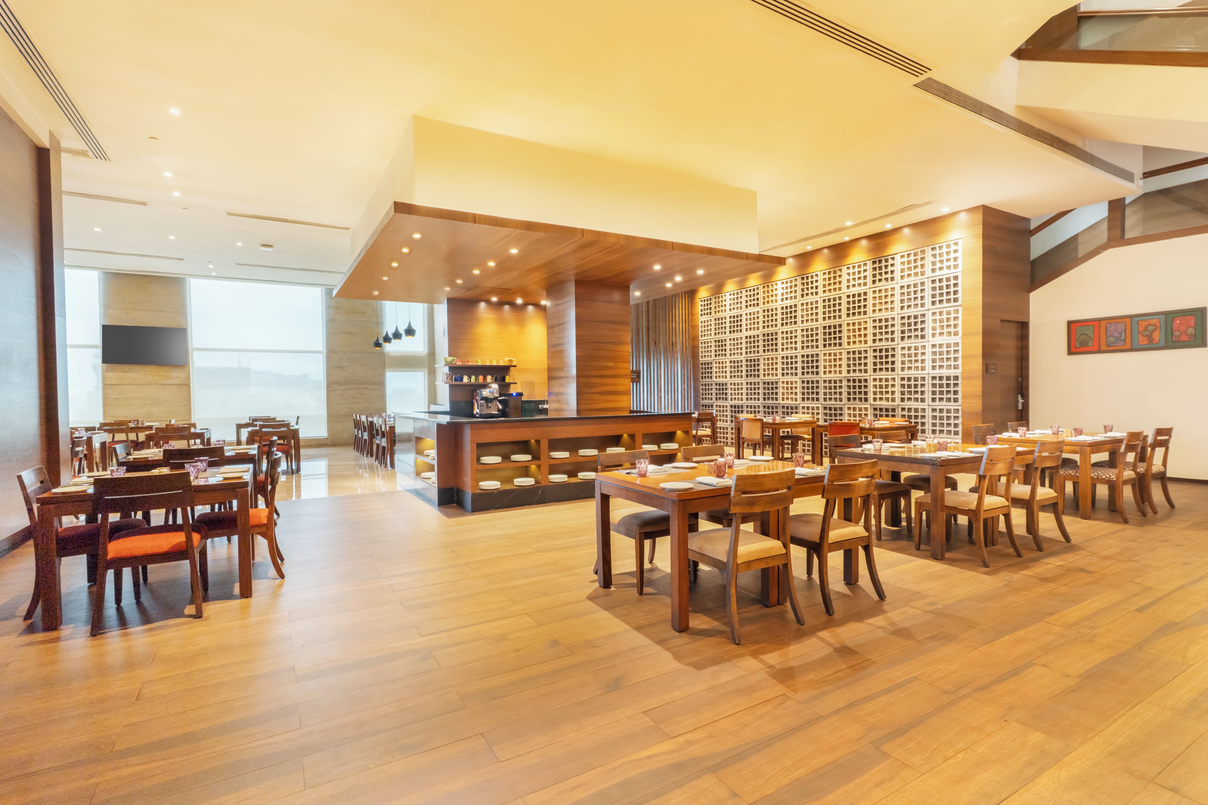 A spacious restaurant with multiple dining tables and chairs, a bar area, and a wall with a patterned design.