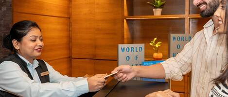 A hotel reception desk with a wooden finish, a name tag, and a sign that reads 'WORLD OF HOTEL'.