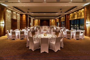 Un amplio salón de banquetes con mesas redondas, sillas blancas y una alfombra estampada.