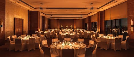 A banquet hall with round tables set for dining, featuring a central floral arrangement and candles.